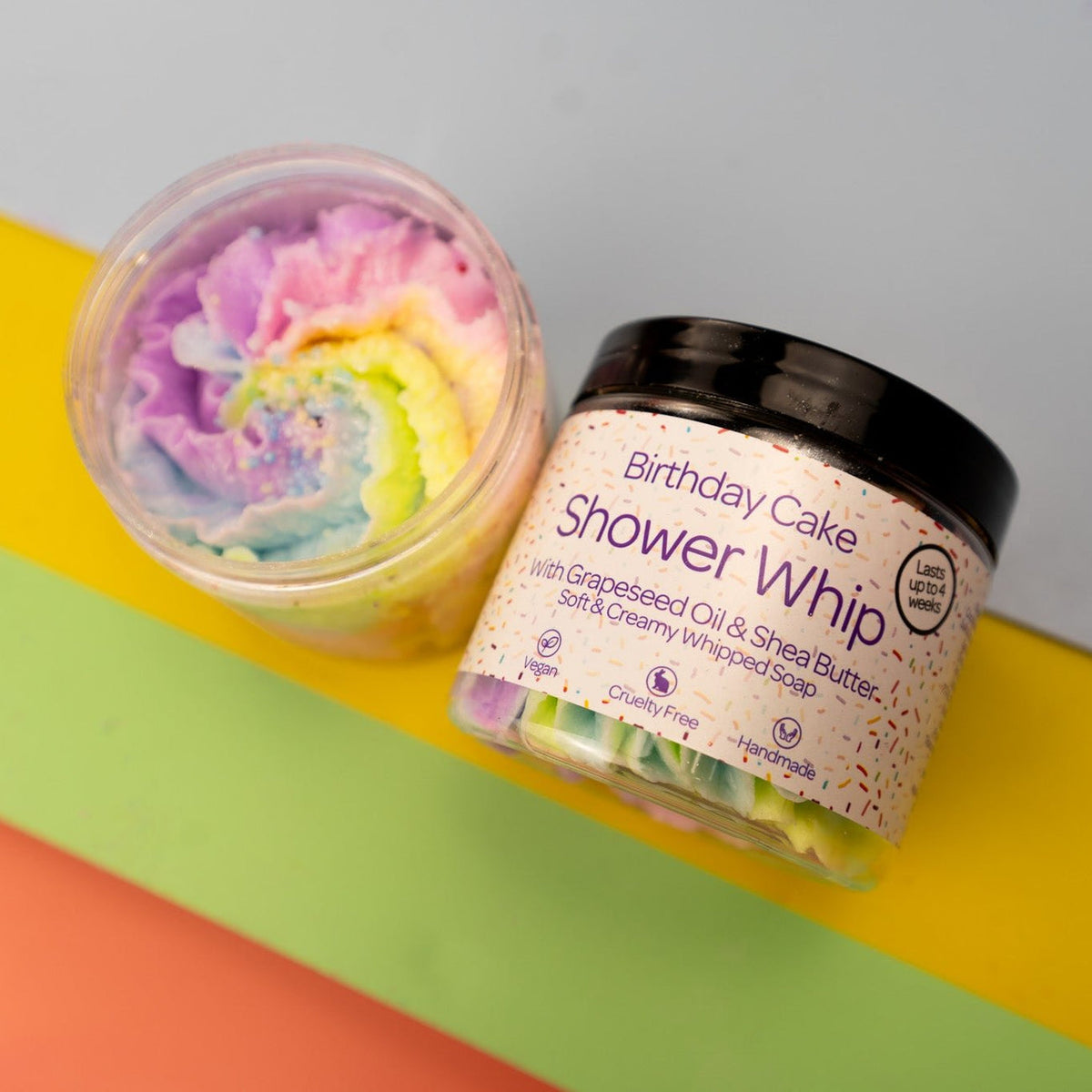 Shower whip soap with rainbow swirl and branded container on a colourful background by Stellia Beauty