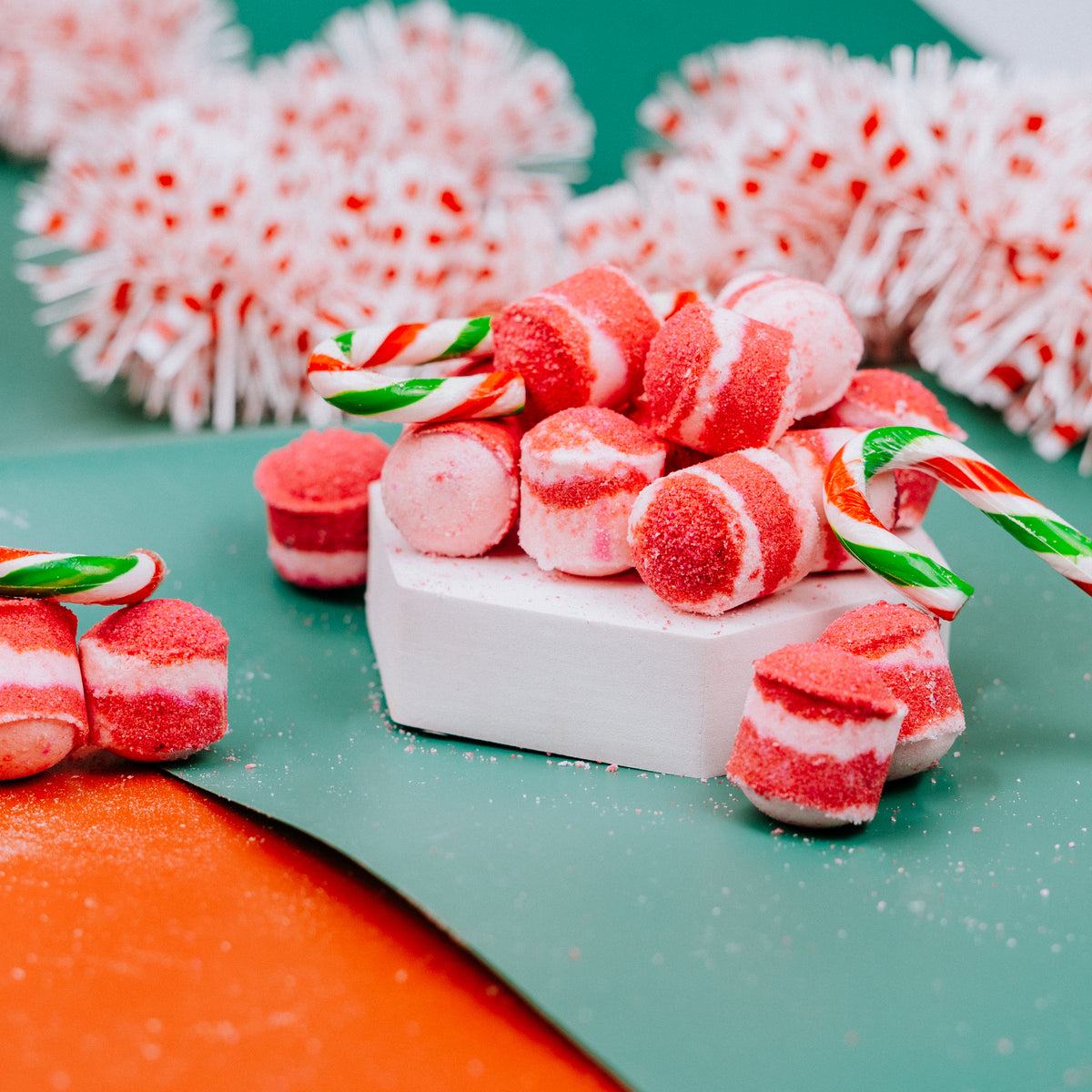 Red and white candy cane bath bombs on a green surface with decorative elements. Stellia Beauty