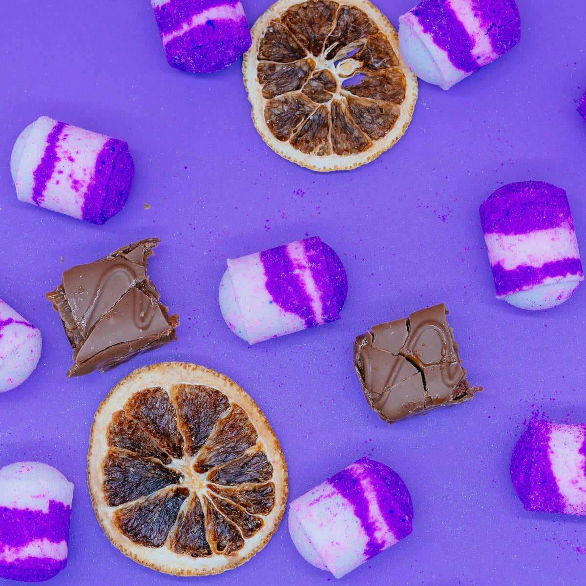 Purple and white striped marshmallows with chocolate pieces and dried oranges on a purple background by Stellia Beauty