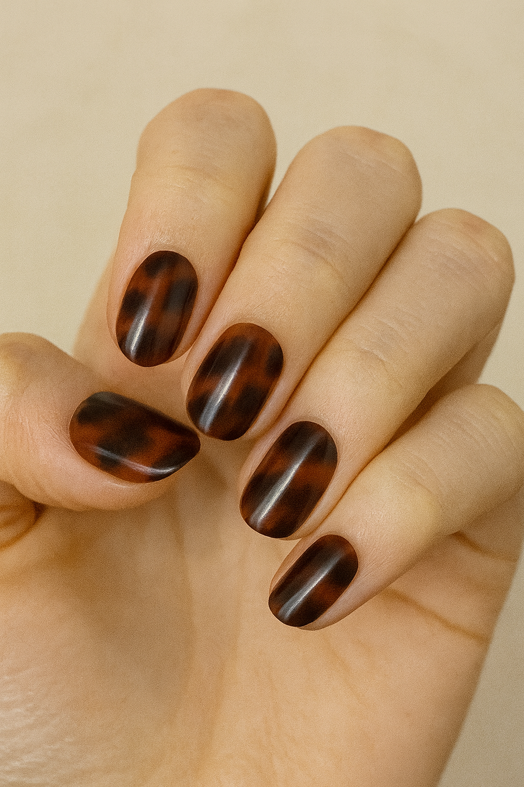 Hand with tortoiseshell nail wraps on a beige background by Stellia Beauty