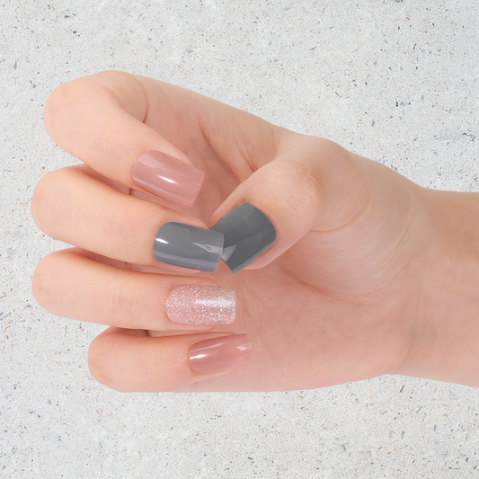 Hand with grey, glitter and pink nail wraps on a light grey background by Stellia Beauty