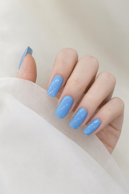 Hand with glossy blue gel nail wraps on a neutral background by Stellia Beauty