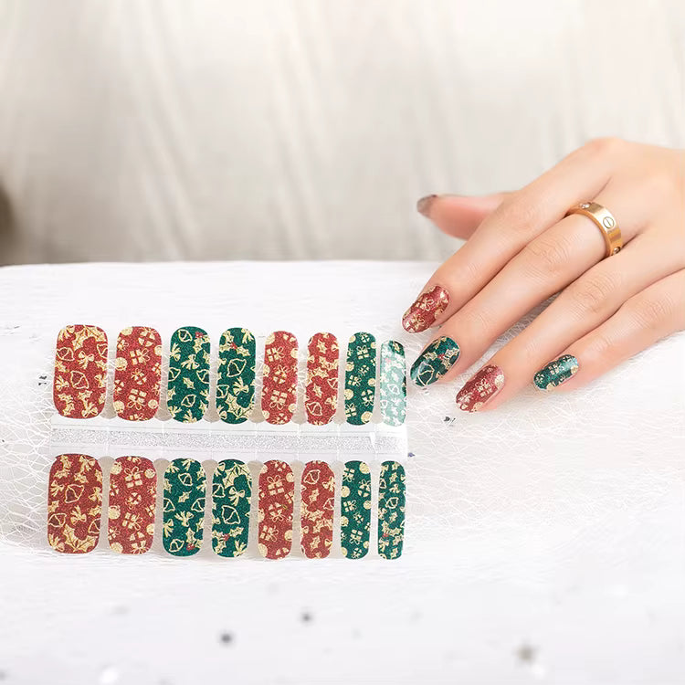 Hand holding a set of festive red and green nail wraps with matching wraps applied on fingernails, showcasing a sparkly gold floral pattern perfect for the holiday season by Stellia Beauty
