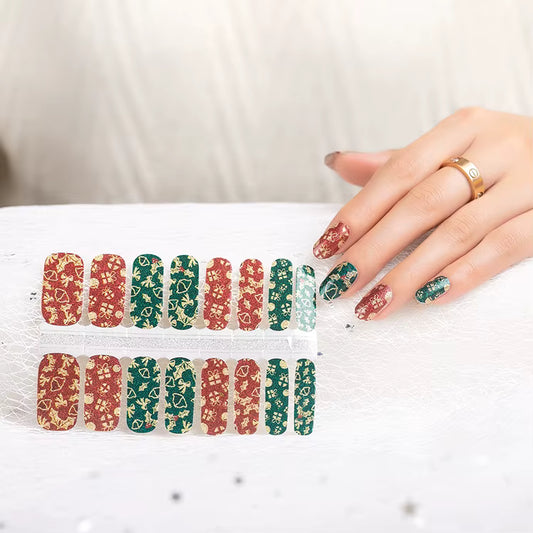 Hand holding a set of festive red and green nail wraps with matching wraps applied on fingernails, showcasing a sparkly gold floral pattern perfect for the holiday season by Stellia Beauty