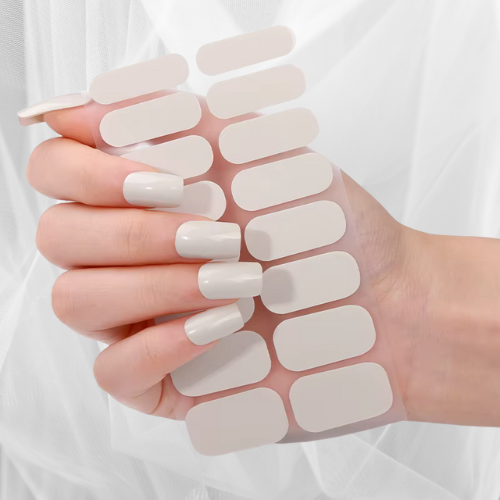 Hand showing glossy ivory beige nail wraps with matching nail wrap sheet – minimalist manicure style