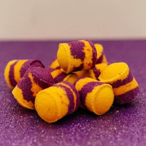 Passion Fruit Martini Mini Bath Bombs Purple and yellow striped cylindrical objects on a purple textured surface by Stellia Beauty