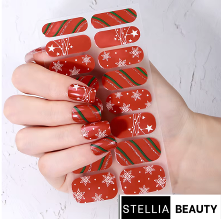 Hand holding a set of red Christmas-themed nail wraps with white snowflakes and green stripes, branded 'Stellia Beauty'.