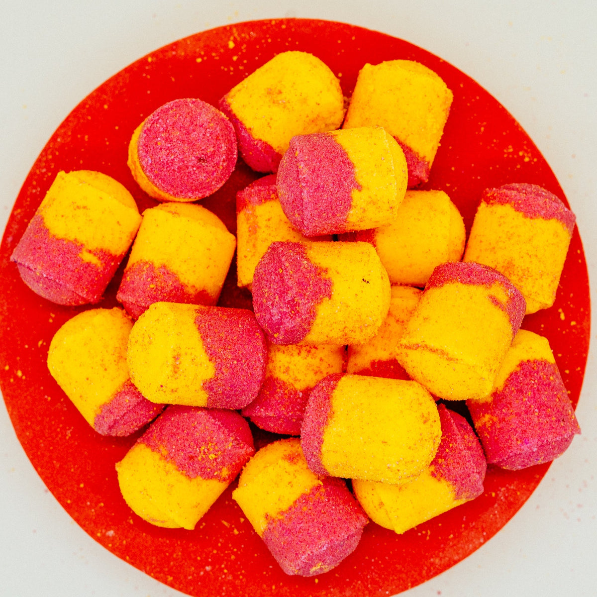 Rhubarb & Custard Mini Bath Bombs Pink and yellow mini bath bomb on a red plate by Stellia Beauty
