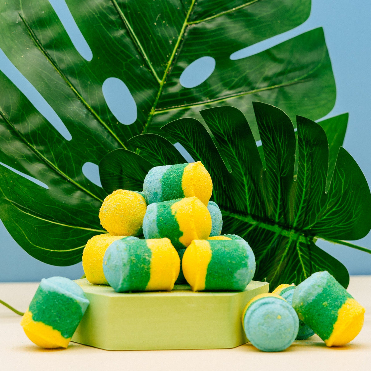 Thai Lime & Mango Mini Bath Bombs Green and yellow candies on a stand with tropical leaves in the background by Stellia Beauty