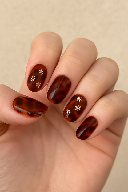 Hand with tortoiseshell nail design featuring white floral patterns on a beige background by Stellia Beauty