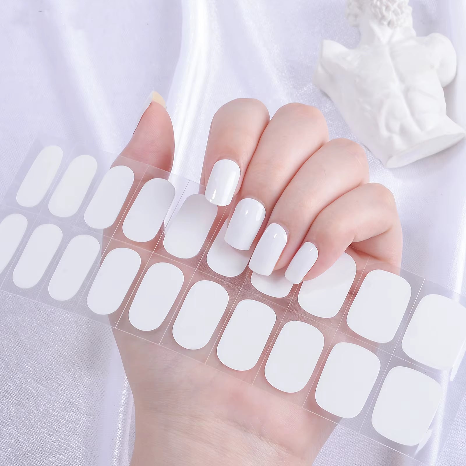 White gel nail wraps being applied to a hand with a white background by Stellia Beauty