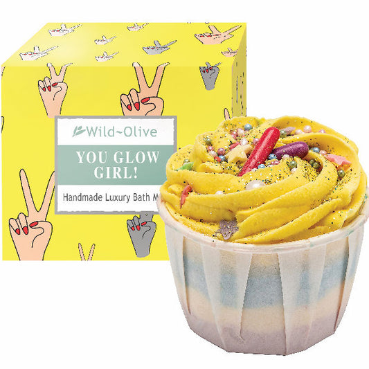 Yellow bath bomb with colourful sprinkles in a cupcake-shaped container, next to a yellow box with 'Wild Olive' branding. Sold by Stellia Beauty